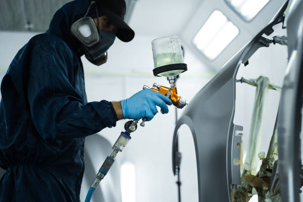 istock Car painter is finishing his paintwork on vehicle by applying lacquer with paint sprayer. Using LVLP spray gun to spread lacquer on metal. 2170063628