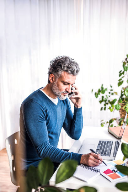 istock Man phone calling and writing notes in planner, working at desk from home. Telecommuting and home office. 2170088965