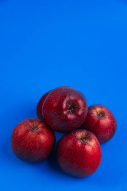 A group of red apples is showcased against a vibrant blue background. Perfect for themes related to fruit, freshness, and bold color contrasts.