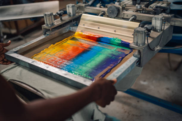 istock Close up of diverse graphic worker's hands silkscreen printing on machine 2170097481