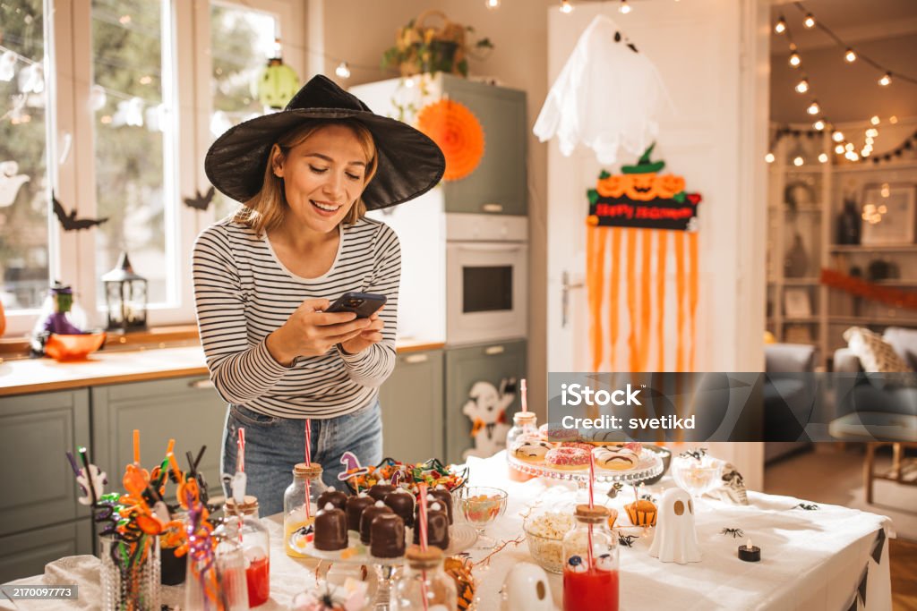 Woman preparing food table for Halloween Mature woman in costume setting table for Halloween lunch, she is photographing it with smart phone. Autumn Stock Photo Woman preparing food table for Halloween Mature woman in costume setting table for Halloween lunch, she is photographing it with smart phone. Autumn Stock Photo