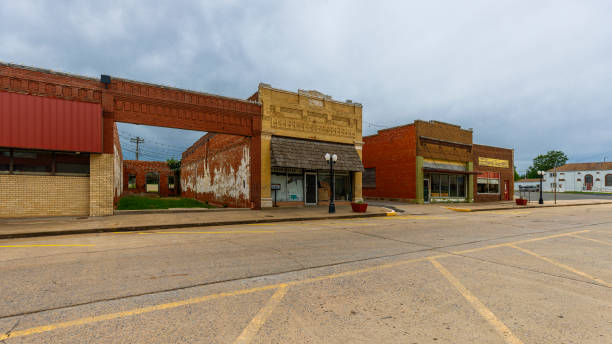Economic decline and empty streets of small Oklahoma town. Deserted storefronts line quiet street in rural Geary in Blaine County Geary, Blaine County, Oklahoma, USA - May 30, 2024: Row of dilapidated storefronts lines a deserted main street in a small town Geary in Oklahoma. Brick buildings with faded paint and boarded windows show signs of neglect and abandonment. Empty street with faded yellow lines stretches out in front, while overcast skies loom above. Scene captures economic struggles and population decline facing many rural communities across America. run down neighborhood stock pictures, royalty-free photos & images
