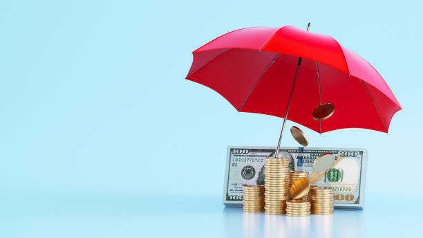 istock Dollar banknotes and coins stacks under red umbrella on blue background 2170108589