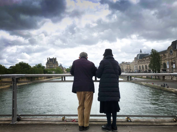 Paris, France - Nov 09 2011: Two men stand on a stone embankment overlooking the Seine River with a barge passing by and buildings lining the riverbank