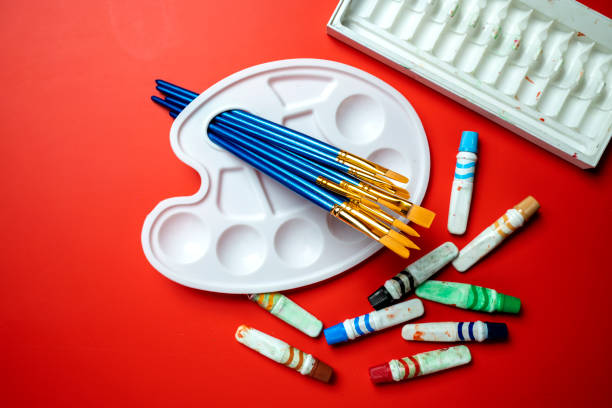 A white palette with a blue brush on it and a bunch of crayons on a red background