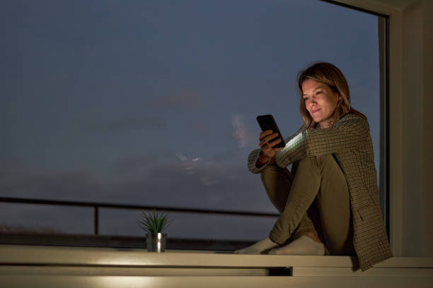 istock Smiling woman using cell phone by the window at night. 2170125640
