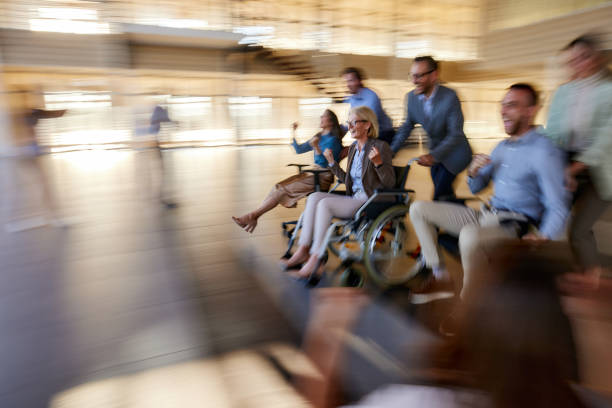 Group of cheerful business colleagues having fun during chair race in the office. Blurred motion. One of them is in a wheelchair.