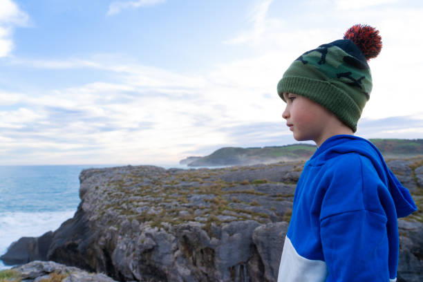 Boy with a woolen hat looking at the landscape from a cliff with copy space