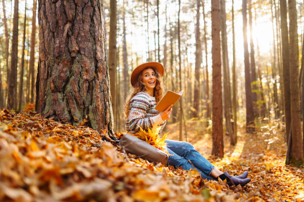 istock A woman enjoys reading in a peaceful forest during autumn while sitting beside her bicycle on fallen leaves. 2170130766