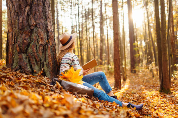 istock A woman enjoys reading in a peaceful forest during autumn while sitting beside her bicycle on fallen leaves. 2170130779