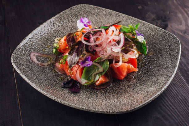 Delicious vegetarian salad with fresh tomatoes, basil, red onions and edible flowers seasoned with olive oil on a gray plate