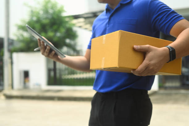 istock Delivery worker in blue shirt using digital tablet next to a vehicle filled with packages. Shipping and delivery services concept 2170134391