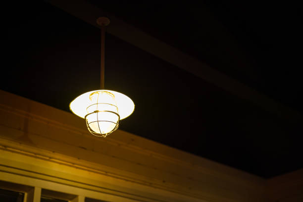 An iron retro style round ceiling lighting lamp is glowing in orange warmlight shade with dark environment background. Interior decoration object, close-up and selective focus.