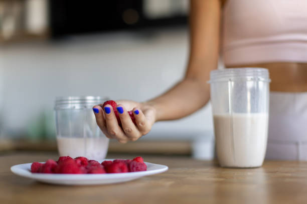 Attractive mid-adult woman dressed in sports clothes, preparing raspberry smoothie in her kitchen, getting ready for a new day.