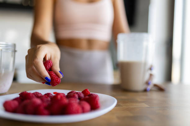 Attractive mid-adult woman dressed in sports clothes, preparing raspberry smoothie in her kitchen, getting ready for a new day.