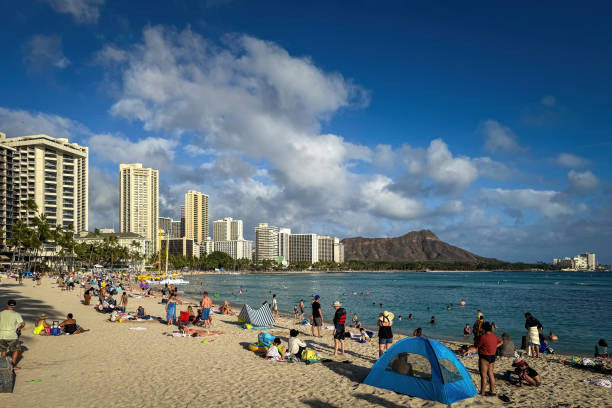 Honolulu, Hawaii, USA - April 2, 2024: Crowded Waikiki Beach against blue sky with clouds