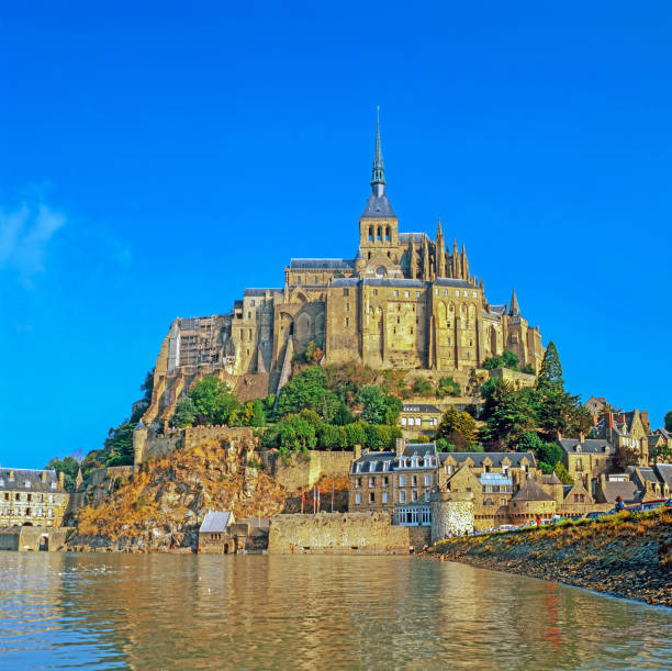 Mont Saint-Michel on tidal Island under sunny summer skyscape. Aerial Drone Point of view from the Atlantic Ocean Side over Mont Saint Michel towards the Normandy Coast. Mont Saint-Michel, Avranches, Manche, Normandy, France, Europe