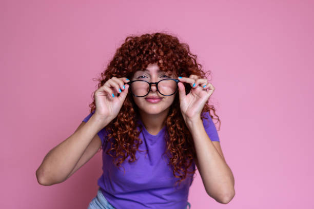 istock Redhead woman with glasses touching her frames on pink background 2170144711