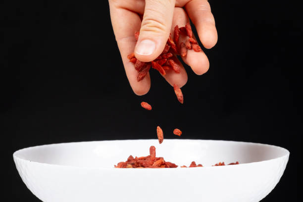 Hand pouring dried goji berries into a plate on a black background