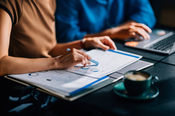 Business Team Analyzing Financial Data in Modern Office Two colleagues reviewing financial data and charts. The focus is on teamwork and analytical skills in a modern office setting with a laptop and coffee. blue business stock pictures, royalty-free photos & images