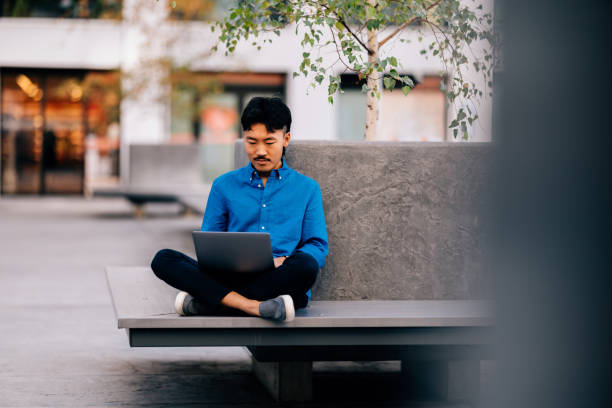 Asian Man Working on Laptop Outdoors in a Relaxed Setting