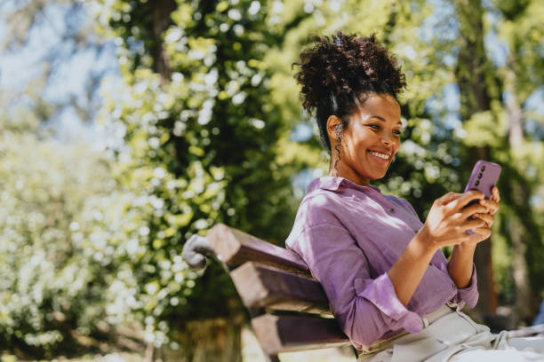 Smiling Woman Relaxing on Park Bench Using Smartphone Outdoors