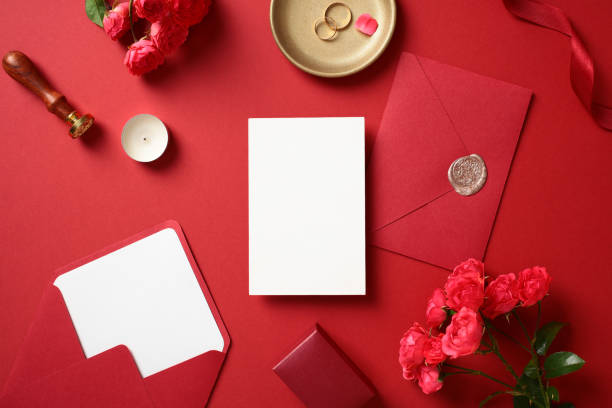 istock Luxury wedding stationery set. Romantic flat lay composition with blank paper card, wedding envelopes, red roses, candle, wax seal stamp and golden rings on a red background. 2170148825