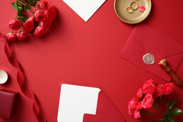 istock Romantic flat lay with roses, sealed envelope, and wedding rings on a red background 2170148990