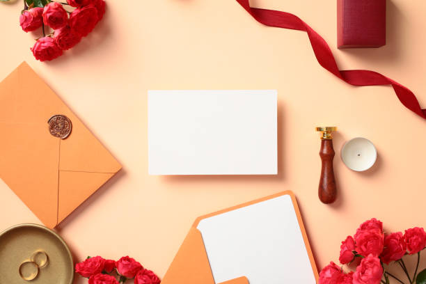 istock Wedding stationery set top view. Elegant flat lay composition with blank paper card, wedding rings, envelopes, red roses, wax seal stamp, candle on pastel beige background. 2170149204