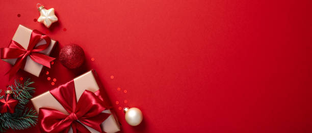 istock Christmas banner design with gifts and decorations on a red background, featuring elegant ribbons, sparkling baubles, and green fir branches 2170154399