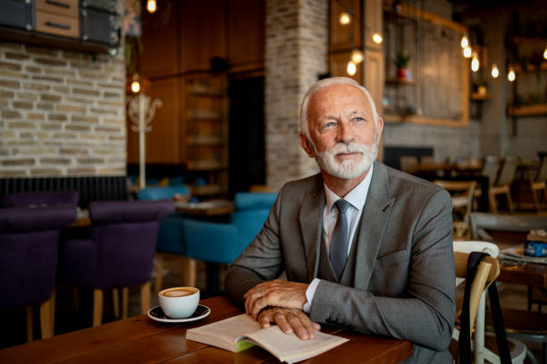 istock Elderly man in modern cafe reading a book and drinking coffee. 2170156077