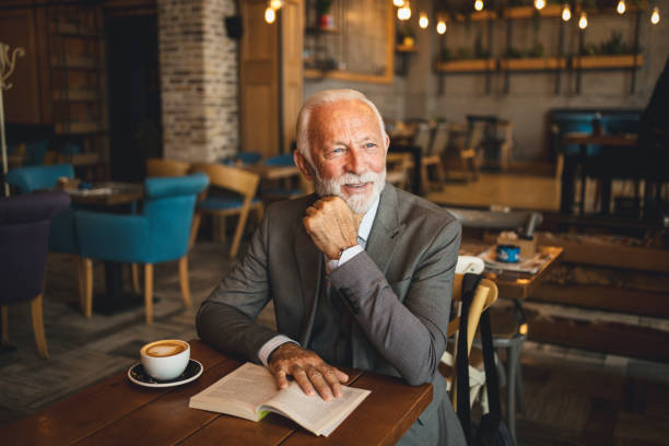 Elderly man in cafe with coffee cup and open book smiling.