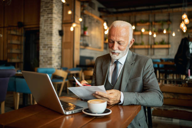 istock Elderly man reviewing documents with laptop in cafe 2170156126