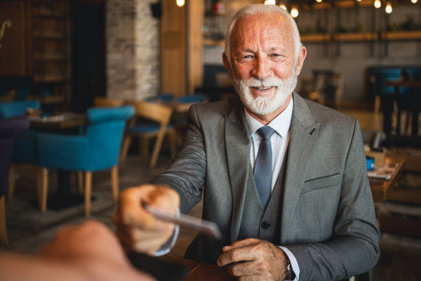 istock Senior man handing out a card in a cozy cafe environment 2170156203
