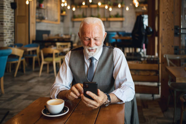 istock Elderly man in suit using smartphone at a cafe table 2170156334