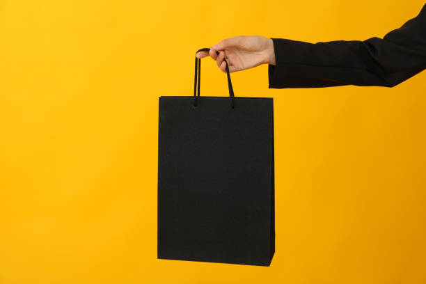 istock Paper shopping bag in hand on yellow background. 2170162162