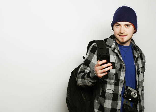 life style, education and people concept: young  man listening to music and using smartphone, while standing against grey background.