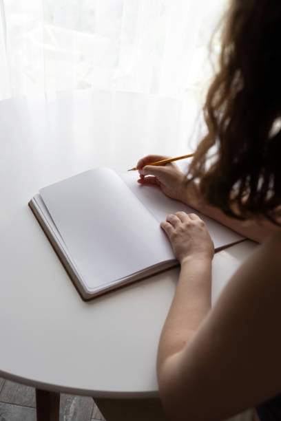 istock Woman holding pencil over blank notebook by a window 2170177592