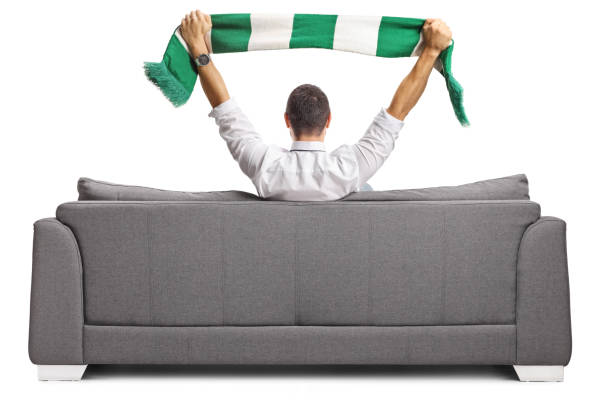 istock Man sitting on a sofa and cheering with a green and white scarf 2170182075