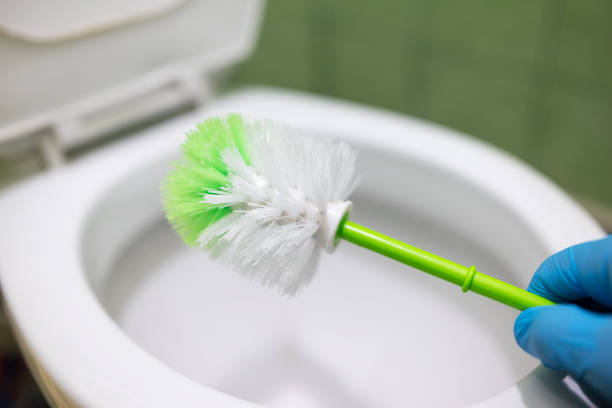 Hand of a man with cleaning brush and toilet on the background