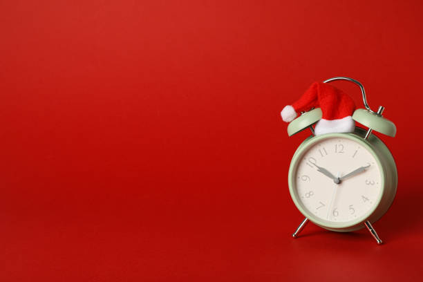istock A clock in a Santa hat on a red background. 2170187755