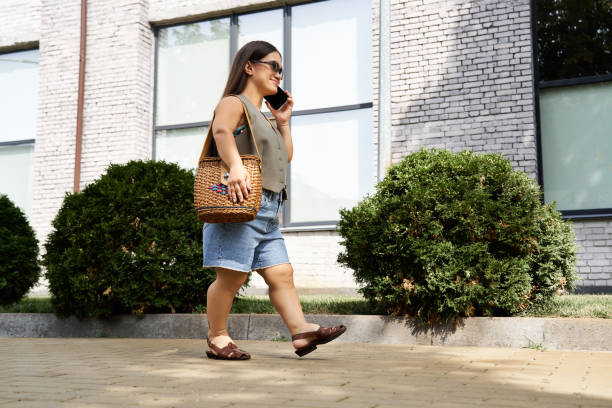 Brunette young woman with short stature enjoying a sunny day outdoors while walking with a woven bag