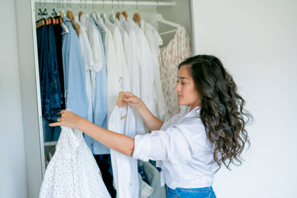 istock Young dark-haired curly beautiful woman is sorting things in large spacious closet. Home organization. Washing things. Analysis of clothes by season. 2170207221