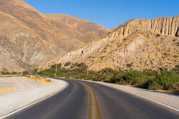 A stone wall leads toward the colorful hills of Purmamarca, Argentina, showing layered mineral textures beneath a clear sky.