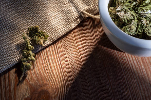 Close-up of dried herbs placed on a burlap cloth and wooden table, with natural light casting shadows.