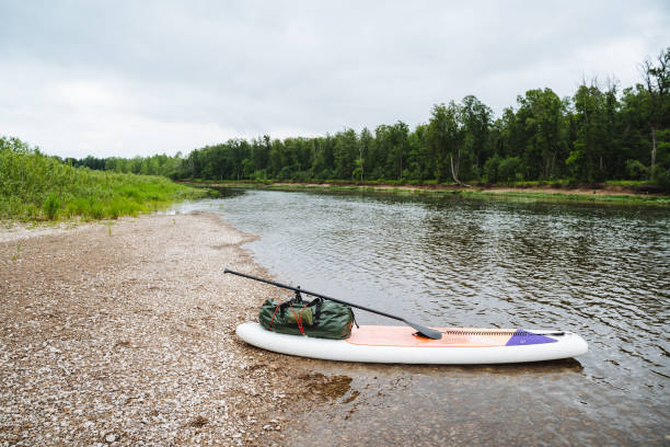 istock A peaceful scene by a riverbank with a paddleboard and gear under cloudy skies, surrounded by lush forest and serene waters, ideal for relaxation and outdoor exploration 2170219488