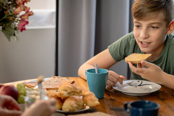 istock Early morning before work. Healthy breakfast preparation. Happy boy spreading peanut butter cream over slice wholegrain bread. 2170225252