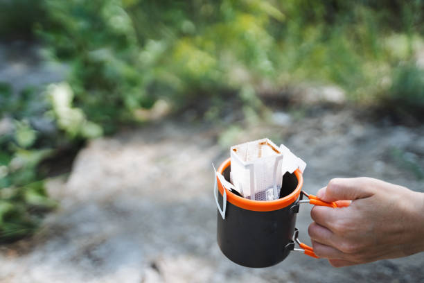 istock A person enjoying the outdoors, drinking coffee and holding a coffee bag. The scene includes keywords like Drinkware, Tableware, Drink, Recreation, Landscape, Eyewear, and Fire 2170226824