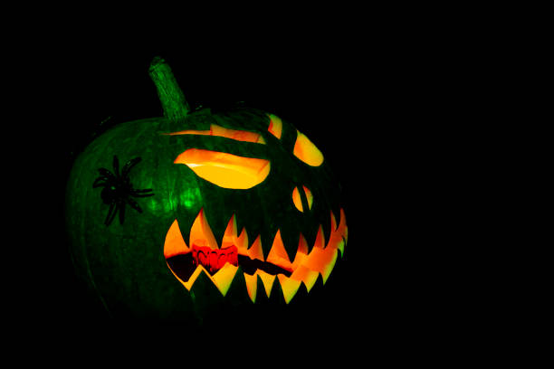 A pumpkin with a spider on it and a scary face. The pumpkin is lit up with a green light and glowing in the dark