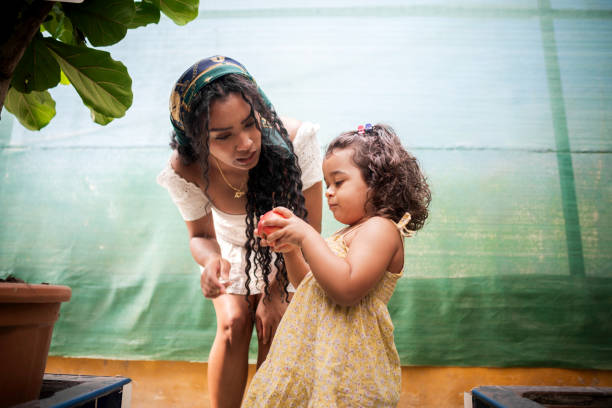 Young mother is crouching, talking to her daughter who is holding a red apple